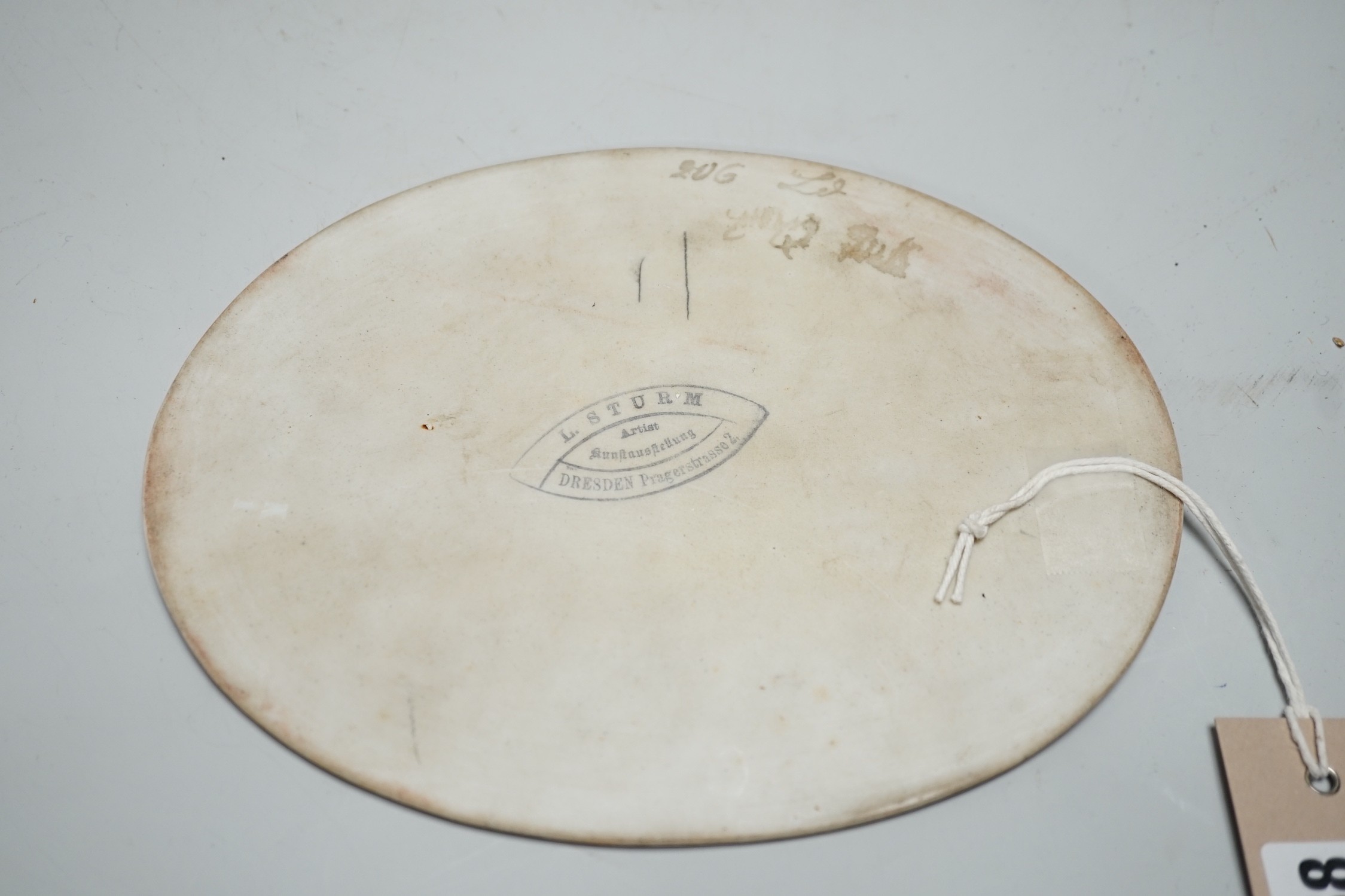 A 19th century painted porcelain oval plaque of a reclining lady reading a book. The reverse stamped L. Sturm Dresden. 15x19.5cm